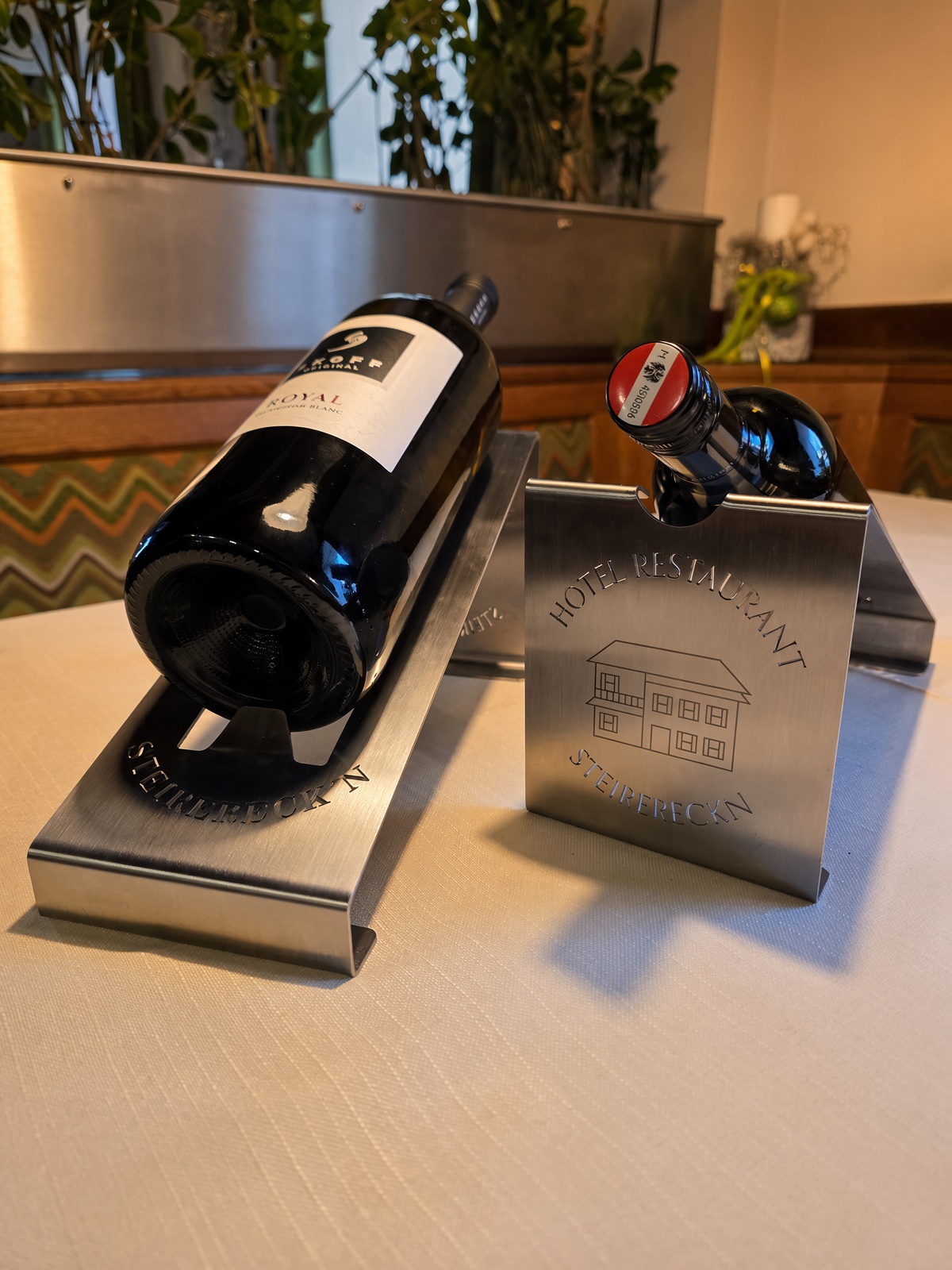 Zwei Flaschenhalter aus gebogenem Edelstahl mit gravierter Hausansicht des Hotel Restaurant Steirereck’n