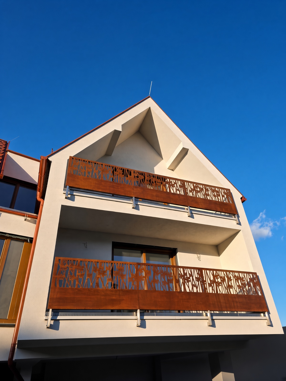 Balkongeländer mit Corten-Füllungen im Blütenmotiv an einem Giebelhaus, Abendlicht